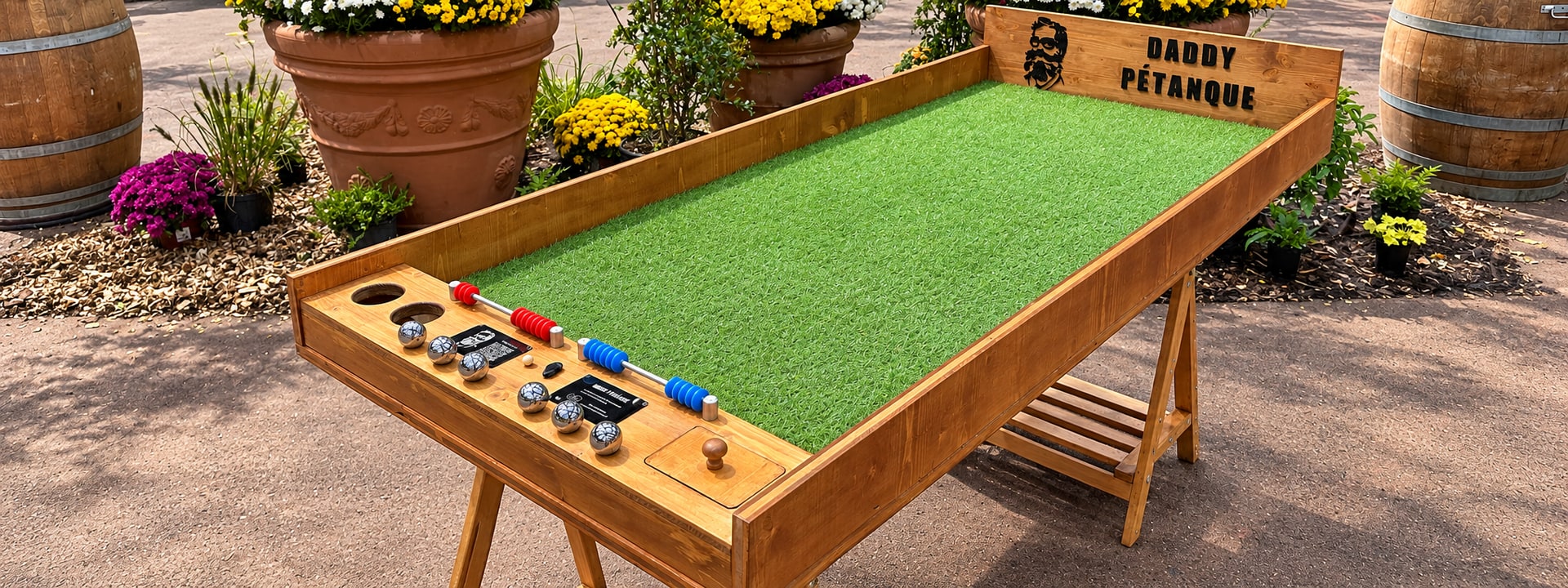 Table de mini-pétanque en bois, entourée de fleurs et de tonneaux